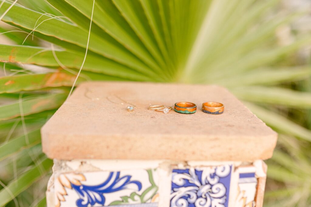 The bride and groom's wedding rings resting on a textured stone tile, with a palm leaf in the background, capturing the essence of their Ibiza elopement